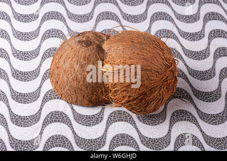 In der Nähe von zwei coconut Hälften fest zusammen auf der schroffen Texturierte braun Shell auf einem Muster Oberfläche Hintergrund mit Haare heraus. Stockfoto