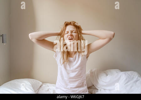 Schlechte Morgen. Stirnrunzelnd Blondine im Bett mit Hände auf das Gesicht. Junge Frau Probleme mit früh aufstehen am Morgen Stockfoto