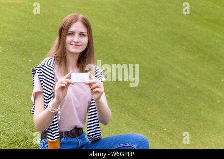 Weibliche Hand, die eine Visitenkarte. Mockup Papier Karte Hinweis auf grüne Blätter Hintergrund. Natur Konzept. Stockfoto