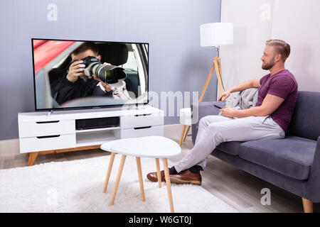 Mann sitzt auf einem Sofa mit Fernbedienung in der Hand halten Stockfoto