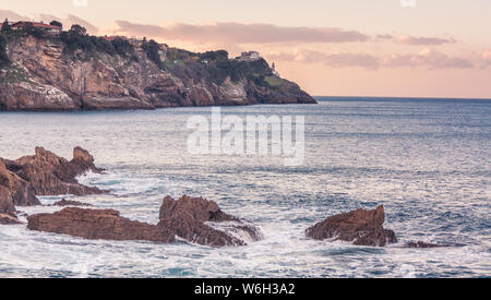 Mundaka, Baskenland, Spanien: 24. November 2012: Felsen im Vordergrund und ein Leuchtturm in der Ferne von einem Sonnenuntergang auf die zerklüftete Küste im Norden Stockfoto