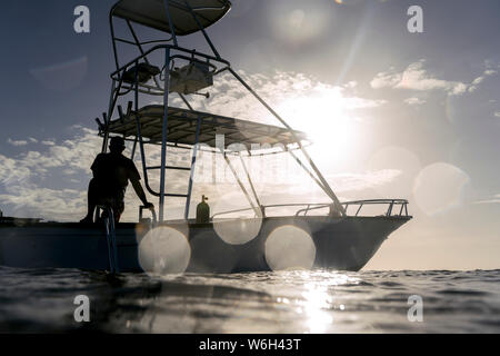 Silhouette eines Mannes auf dem Deck des Bootes auf dem Wasser gegen einen blauen Himmel mit Sonnenlicht, Bay Islands, Honduras Stockfoto