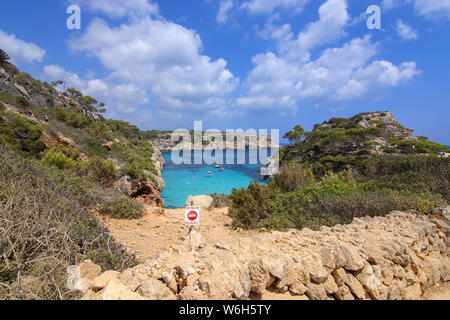 CALO DES MORO, MALLORCA, SPANIEN - 27. JULI 2019: Warnschild durch kleine extrem Turquoise Bay und steilen Klippen an einem sonnigen Tag am 27. Juli 2019 in Calo Stockfoto