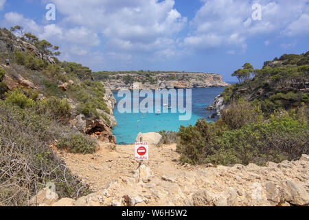 CALO DES MORO, MALLORCA, SPANIEN - 27. JULI 2019: Warnschild durch kleine extrem Turquoise Bay und steilen Klippen an einem sonnigen Tag am 27. Juli 2019 in Calo Stockfoto