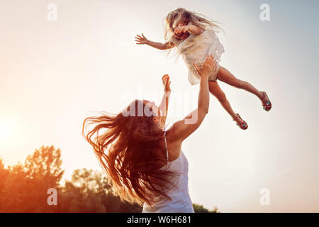 Frau spielen und Spaß mit Tochter im Sommer Park bei Sonnenuntergang. Mutter wirft Mädchen im Freien. Muttertag Stockfoto