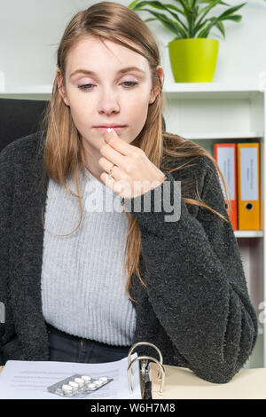 Eine junge Frau in das Amt nimmt Pillen gegen ihre Kopfschmerzen Stockfoto