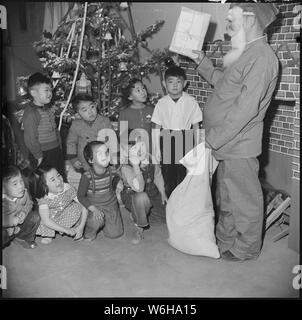 Granada Relocation Center, Amache, Colorado. In seinem Santa Claus Maske, tragen ein Paar der roten Schlafanzug. . .; Umfang und Inhalt: Der vollständige Titel für dieses Foto lautet: Granada Relocation Center, Amache, Colorado. In seinem Santa Claus Maske, tragen ein Paar der roten Schlafanzug, Chief Steward Matsumoto von Block 7-H des Granada Relocation Center war Santa Claus für Heiligabend. Die Kinder hatten keine Bäume in ihrer Kaserne Zimmer Wohnungen, aber jede Messe einen Weihnachtsbaum und Geschenke, viele aus kirchlichen Gruppen im ganzen Land schickte, wurden an die Kinder verteilt. Stockfoto