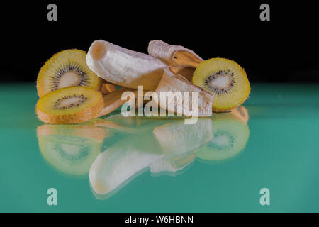 Köstlichen tropischen Snack - Bananenscheiben und grün Kiwi auf einem grünen Tisch und schwarzem Hintergrund - nahrhaft und lecker Stockfoto