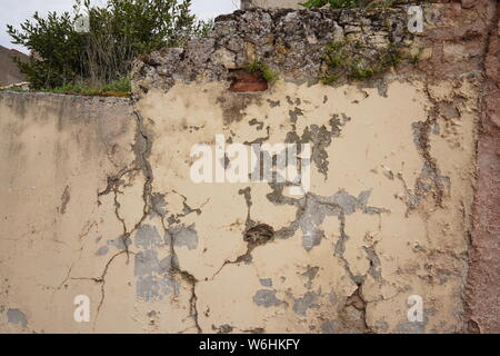 Rissiger und abblätternder Putz an der Wand eines teilweise verfallenen alten Hauses mit einem Strauch, der oben wächst, Sigüenza, Spanien Stockfoto