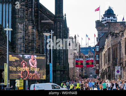 Royal Mile, Edinburgh, Schottland, Großbritannien, 1. August 2019. Bereits am Tag vor der offiziellen Eröffnung des Fringe-Festivals ist das Zentrum der Stadt entlang ihrer Haupttouristenroute mit Besuchern angeveist. Das Hauptquartier des Edinburgh International Festivals, The Hub on Castlehill mit einem großen Plakat, das für ein Theaterstück namens The Secret River wirbt Stockfoto