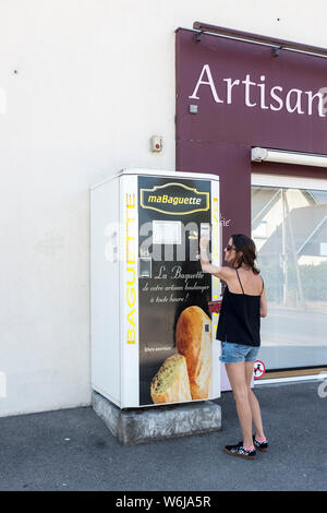 Eine Frau setzt Geld in einem Automaten abfüllen Baguettes außerhalb einer Bäckerei in Coueron, Frankreich Stockfoto