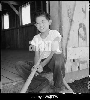 Manzanar Relocation Center, Manzanar, Kalifornien. Umsiedler Boy wartet am Eingang des Recrea. . .; Umfang und Inhalt: Der vollständige Titel für dieses Foto lautet: manzanar Relocation Center, Manzanar, Kalifornien. Umsiedler Junge am Eingang der Freizeit Hall an diesem Krieg Relocation Authority Center warten. Er ist bestrebt, für das Baseballteam zu montieren. Stockfoto