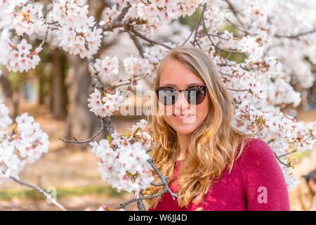 Porträt, junge Frau mit Sonnenbrille, Tourist, zwischen blühenden Kirschblüten, die Kirschblüte im Frühling, Tokio, Japan Stockfoto