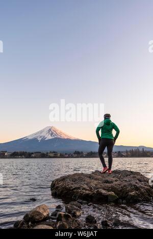 Abendstimmung, junge Frau auf einem Stein im Wasser und der Blick in die Ferne, Blick über Lake Kawaguchi, zurück Vulkan Mt. Fuji, Yamanashi Stockfoto