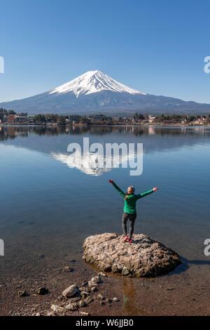 Junge Frau steht auf Stein im Wasser und streckt die Arme in die Luft, See Kawaguchi, zurück Vulkan Mt. Fuji, Yamanashi Präfektur, Japan Stockfoto