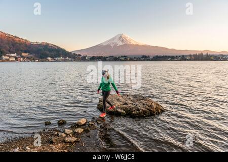 Abendstimmung, junge Frau geht über Steine im Wasser, Blick über Lake Kawaguchi, zurück Vulkan Mt. Fuji, Yamanashi Präfektur, Japan