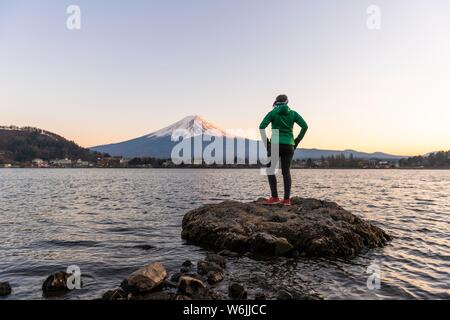 Abendstimmung, junge Frau auf einem Stein im Wasser und der Blick in die Ferne, Blick über Lake Kawaguchi, zurück Vulkan Mt. Fuji, Yamanashi Stockfoto