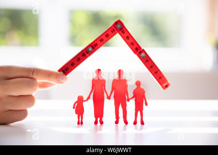 Die Geschäftsfrau schützende Hand rot Familie Figuren mit Dach über reflektierende Schreibtisch Stockfoto