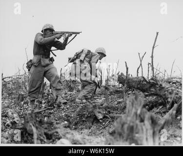 Foto einer Marine, die auf einem japanischen Scharfschützen auf Okinawa; Umfang und Inhalt: Original Bildunterschrift: Ein Marine der 1st Marine Division zeichnet eine Raupe auf einem japanischen Sniper mit seinem Tommy-gun, als sein Begleiter Enten für Decken. Die Abteilung arbeitet an Wana Ridge, bevor die Stadt von Shuri. Von Okinawa, 1945. Stockfoto