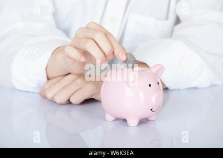 Weibliche hand Amicana Münzen und ein Viertel in ein Sparschwein auf weißem Hintergrund Stockfoto