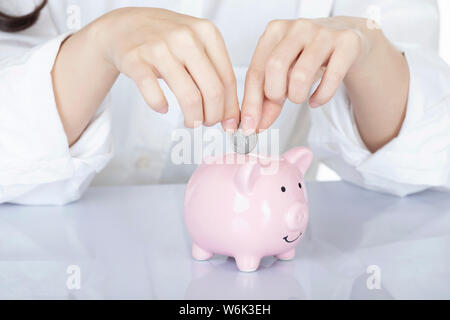 Weibliche hand Amicana Münzen und ein Viertel in ein Sparschwein auf weißem Hintergrund Stockfoto