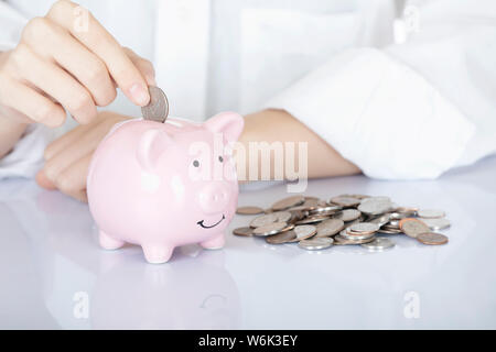 Weibliche hand Amicana Münzen und ein Viertel in ein Sparschwein auf weißem Hintergrund Stockfoto