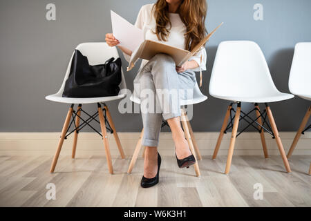Junge Geschäftsfrau Ordner beim Sitzen auf Stuhl warten auf Job Interview Stockfoto