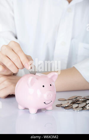 Weibliche hand Amicana Münzen und ein Viertel in ein Sparschwein auf weißem Hintergrund Stockfoto