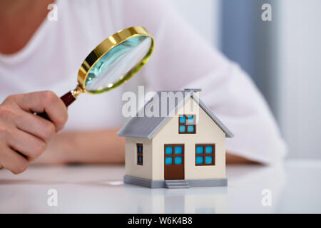 Nahaufnahme einer Hand, die Lupe ist eine Geschäftsfrau Glas über Haus Modell über Weiß Schreibtisch Stockfoto