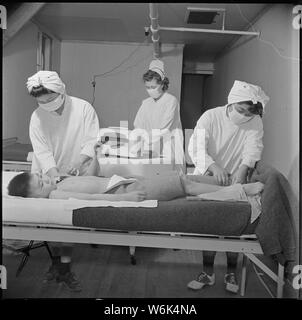 Poston, Arizona. Eingetragene Krankenschwester, Frau Edythe Sasser, wird unterstützt durch Yoshiko Konatsu, Beihilfe, Krankenschwester,. . .; Umfang und Inhalt: Der vollständige Titel für dieses Foto lautet: Poston, Arizona. Eingetragene Krankenschwester, Frau Edythe Sasser, wird von Yoshiko Konatsu, Hilfe der Krankenschwester unterstützt und Tamiko Kitasaki, Beihilfe, Krankenschwester, in der Behandlung der Kinderlähmung. Alle Patienten leiden unter dieser Dread Disease werden von der Kenny Methode behandelt. Hot Packs sind um die betroffenen Gliedmaßen angewendet, und dies wird durch Muskel- und Nervensystem Umerziehung gefolgt. Stockfoto