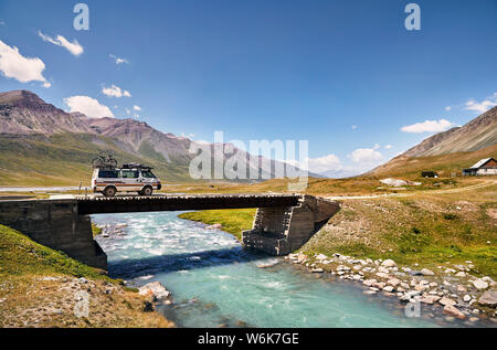 Weiß van mit dem Fahrrad auf dem Dach, überquert den Fluss über eine Brücke in den Bergen in Kirgisistan Stockfoto