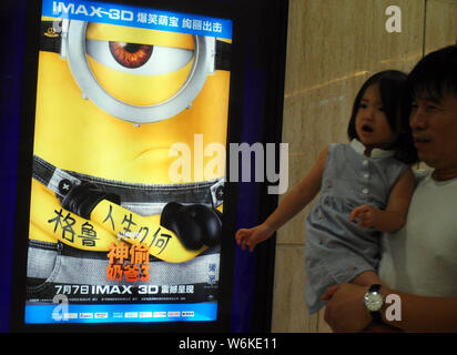 ---- Eine Chinesische filmgoer seine Tochter holding Spaziergänge hinter einem Plakat des Films "espicable Me3" in einem Kino in Kunshan City, Central China Hubei Stockfoto