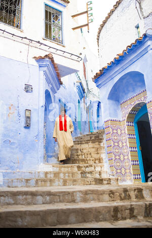 Eine marokkanische alter Mann, das Tragen der traditionellen Djellabah ist ein Spaziergang durch die engen Gässchen von Chefchaouen, Marokko. Stockfoto