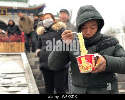 Ein chinesischer Dorfbewohner frisst Master Kong Instant Nudelsuppe wie er Warteschlangen bis Chinesische Zeichen "Fu", das heisst, Vermögen oder Glück in englischer Sprache zu erhalten, geschrieben Stockfoto