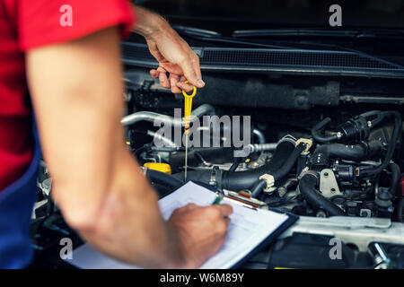 Auto Inspektion und Wartung - Mechaniker den Ölstand im Motor prüfen und Schreiben in Checkliste Stockfoto