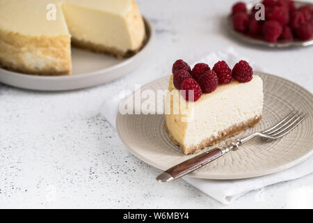 Scheibe des klassischen New Yorker Käsekuchen mit Himbeeren auf weiße Platte. Detailansicht. Home Bäckerei Konzept / Stockfoto