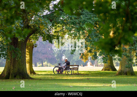 Northampton GROSSBRITANNIEN. 2. August 2019. Wetter. Einen warmen, sonnigen Morgen für diese Radfahrer, der eine Entlüftung auf der Parkbank in Abington Park, lange Schatten durch die niedrige Sonne verursacht, Kredit: Keith J Smith./Alamy leben Nachrichten Stockfoto