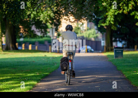 Northampton GROSSBRITANNIEN. 2. August 2019. Wetter. Einen warmen, sonnigen Morgen für diese Radfahrer, reitet die Allee der Bäume in Abington Park in Richtung Park Avenue South, lange Schatten durch die niedrige Sonne verursacht, Kredit: Keith J Smith./Alamy leben Nachrichten Stockfoto