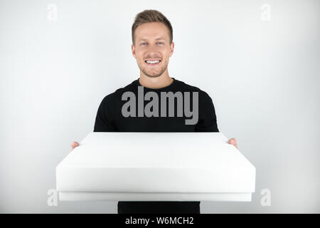 Hübscher junger Mann mit schwarzen T-Shirt holding Paket im Plastiketui für Lieferung auf isoliert weißer Hintergrund Stockfoto