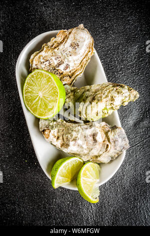 Frische Austern Muscheln mit Zitrone auf einem schwarzen konkreten Hintergrund, Ansicht von oben kopieren Raum Stockfoto
