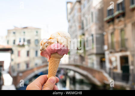 Person's Hand Eis Kegel Vor einem unscharfen alten Häusern in Venedig Stockfoto