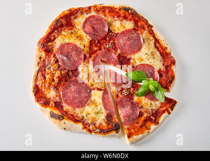 In Scheiben geschnittene Pepperoni Pizza mit frischem Basilikum Blätter, geschmolzenen Mozzarella und Tomatenmark gewürzt mit Kräutern aus gesehen oben auf weißem isoliert Stockfoto