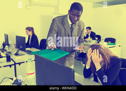Zornigen Mann Chef pointinting zu vermisst in der Arbeit zu Frau Manager am Laptop arbeiten Stockfoto