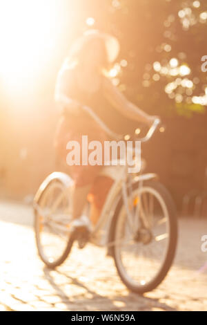 Junge Frau mit Hut unterwegs mit dem Fahrrad an der alten europäischen Street, unscharfes Bild Stockfoto