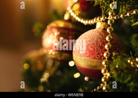 Das Porträt einer christmas ball hängen in einen Weihnachtsbaum mit einem christmas garland daneben und ein paar extra Urlaub Ornamente in den unscharfen zurück Stockfoto