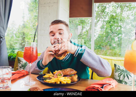 Bild der glücklichen Mann essen vegane Burger in vegane Restaurant oder Cafe. Lächelnd mann am Tisch sitzen. Stockfoto