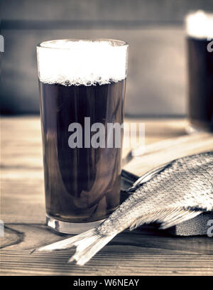 Auf einer hölzernen Tisch zwei Gläser Bier, neben dem Schneidebrett getrockneten Fisch und ein Messer. Stockfoto