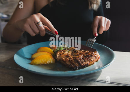 Mädchen Schnitte Saftig gegrillte Putensteak mit Messer und Gabel auf den türkisblauen Platte. Hähnchenfilet. Steak serviert mit karamellisiertem Pfirsich. Stockfoto