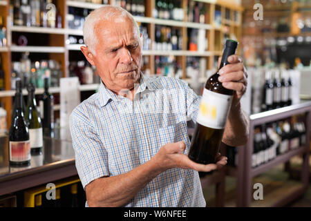 Froh, heiter Grauhaariger alter Mann Auswahl Wein in der modernen Weinladen Stockfoto