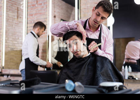 Hübscher junger Mann während Bart rasieren von professionellen Friseur im barbershop Stockfoto
